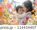 Joyful mother hugging her delighted little girl surrounded by lush garden flowers, celebrating togetherness 114434407