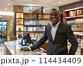 Smiling professional hotel concierge standing confidently at reception desk 114434409