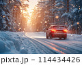 Car driving on a snow-covered road in the forest against the setting sun. 114434426