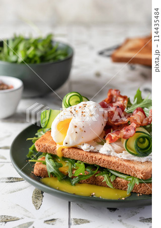 Toasts sandwich with poached egg, cucumber, arugula, bacon and cream cheese on printed tile kitchen background for healthy breakfast Toasts sandwich with poached egg, cucumber, arugula, bacon and cream cheese on printed tile kitchen background for healthy breakfast 114435484
