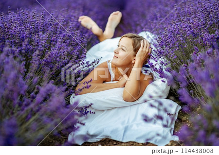 A middle-aged woman lies in a lavender field and enjoys aromatherapy. Aromatherapy concept, lavender oil, photo session in lavender 114438008