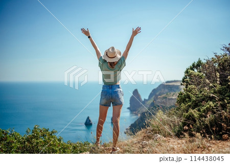 Woman tourist sky sea. Happy traveller woman in hat enjoys vacation raised her hands up Woman tourist sky sea. Happy traveller woman in hat enjoys vacation raised her hands up 114438045