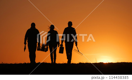 Walking through a field, three farmers are accompanied by their equipment as the sun sets. Walking through a field, three farmers are accompanied by their equipment as the sun sets. 114438385
