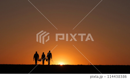 At sunset, three farmers walk through a field, carrying their equipment. At sunset, three farmers walk through a field, carrying their equipment. 114438386