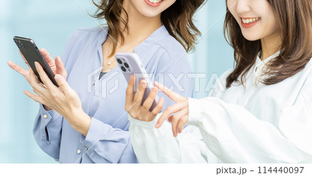 スマホを見て話す2人のビジネスウーマン スマホを見て話す2人のビジネスウーマン 114440097