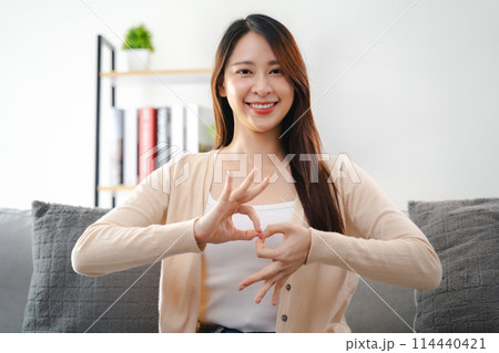 A young deaf woman is sitting on a couch and making a sign Language to communicate. 114440421
