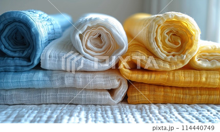 Rolled Up Linen Blankets in Blue, White, and Yellow Hues on a Bed 114440749