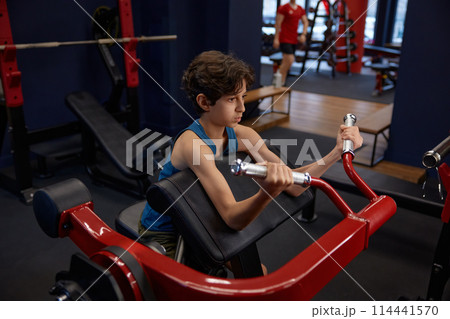 Concentrated boy doing sports exercise for strong arms while training in gym 114441570