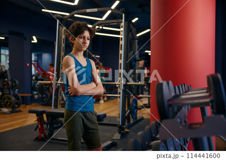 Pensive overwhelmed preteen boy looking at dumbbells having hard choice 114441600