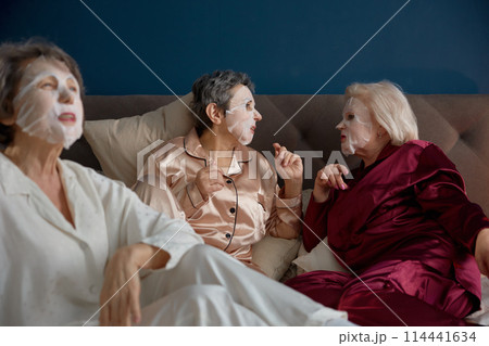 Happy senior female friends with cotton mask on face having nice conversation 114441634