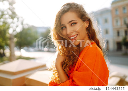 Young woman posing against backdrop of urban landscape in bright orange dress. Concept of lifestyle. Young woman posing against backdrop of urban landscape in bright orange dress. Concept of lifestyle. 114443225
