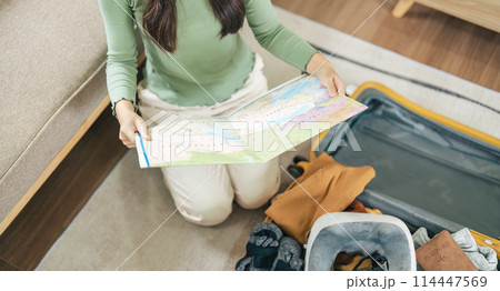 Happy Asian young woman packing suitcase at home. Preparing for summer holiday vacation abroad travel. 114447569