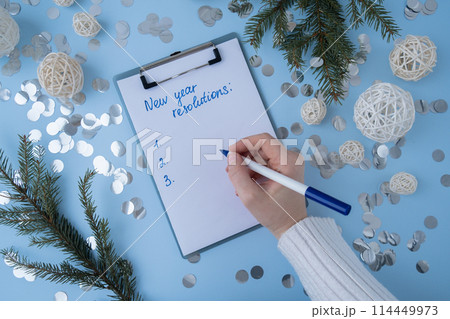 Female hands writing handwritten new year resolutions aims goals on paper notepad. Preparation for New Year. Planning and setting goals for personal development  114449973