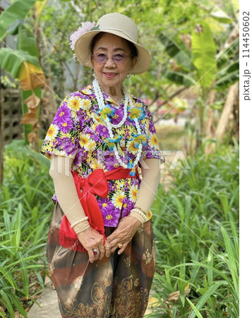 Portrait of smiling Asian senior woman wearing colorful dress and straw hat in the garden. Portrait of smiling Asian senior woman wearing colorful dress and straw hat in the garden. 114450602