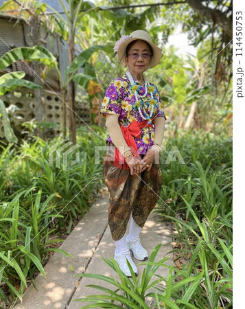 Portrait of beautiful Asian senior woman wearing flower dress standing in garden. 114450753
