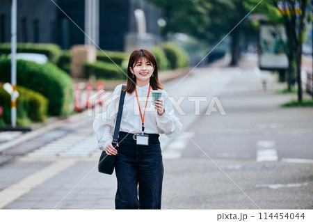 コーヒーカップを持ちながら歩く若い女性 114454044