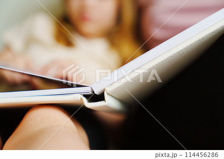 Mother and daughter flip through the pages of a photo book in a white binding. 114456286