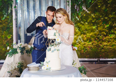 The bride and groom cut the wedding cake at the banquet.  114457108