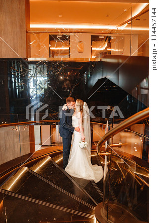 Bride and groom embracing on a golden spiral staircase.  114457144