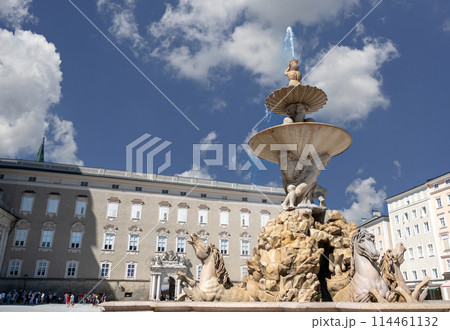 Salzburg, Austria, August 15, 2022. In the center of the Residenzplatz square the beautiful fountain with statues of prancing horses. People walk. 114461132