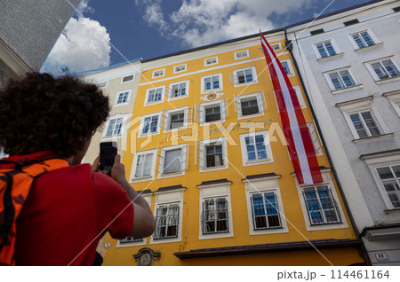 Salzburg, Austria, August 15, 2022. A cute boy is photographing mozart's house with his cellphone as a souvenir of the holiday. Technology use concept. 114461164