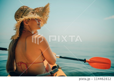 Woman in kayak back view. Happy woman with long hair in a swimsuit and hat floating in kayak on the sea. Summer holiday vacation. Summer holidays vacation at sea. Woman in kayak back view. Happy woman with long hair in a swimsuit and hat floating in kayak on the sea. Summer holiday vacation. Summer holidays vacation at sea. 114462812