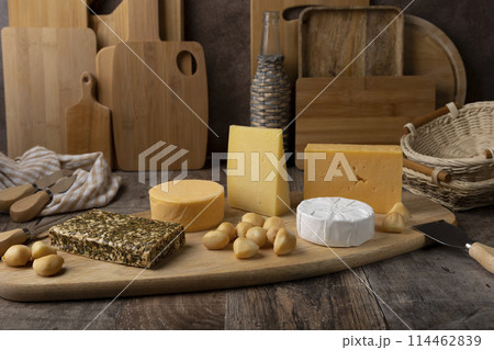 Cheese assorted on a wooden board, rustic style. Several varieties of whole cheese: parmesan, tilsiter, halloumi with spices, camembert, smoked bocconcini, cheddar. Cheese plate. Cheese assorted on a wooden board, rustic style. Several varieties of whole cheese: parmesan, tilsiter, halloumi with spices, camembert, smoked bocconcini, cheddar. Cheese plate. 114462839