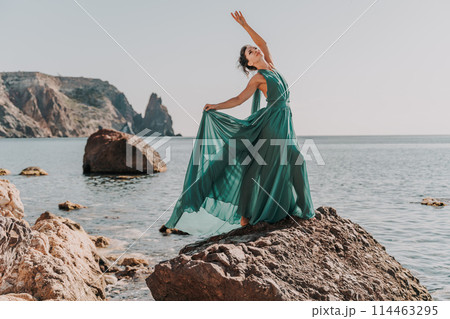 Woman green dress sea. Woman in a long mint dress posing on a beach with rocks on sunny day. Girl on the nature on blue sky background. 114463295