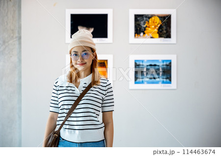 Visitor woman smiling on art gallery collection in front framed paintings pictures on white wall, lifestyle Asian people watch at photo frame to leaning against at show exhibition artwork gallery 114463674