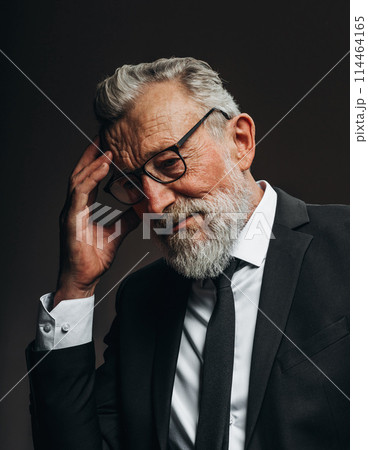 Pensive old actor in formal black suit, keeps palms near his chin. 114464165