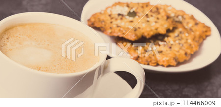 Cup of coffee with milk and fresh baked oatmeal cookies on white plate. Delicious crunchy dessert Cup of coffee with milk and fresh baked oatmeal cookies on white plate. Delicious crunchy dessert 114466009