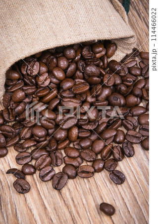 Heap of dark roasted fragrant coffee beans in jute bag 114466022