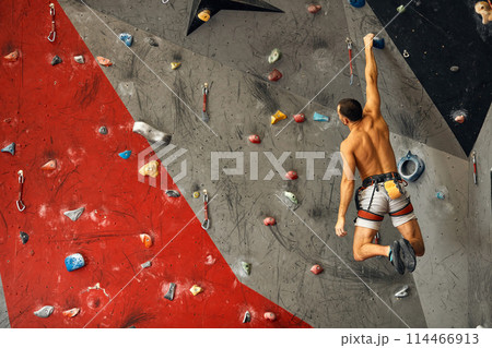 Young man climbing on artificial rock, hanging on safety ropes Young man climbing on artificial rock, hanging on safety ropes 114466913