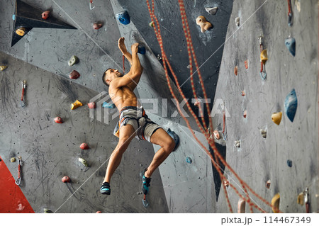 Panoramic man bouldering at an indoor climbing centre. 114467349