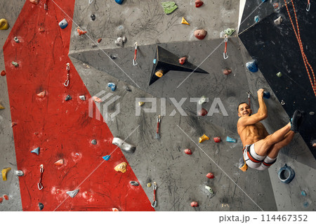 Panoramic man bouldering at an indoor climbing centre. 114467352