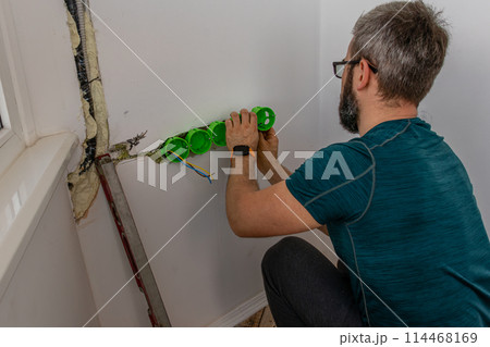 a man mounts wall sockets on plaster 114468169