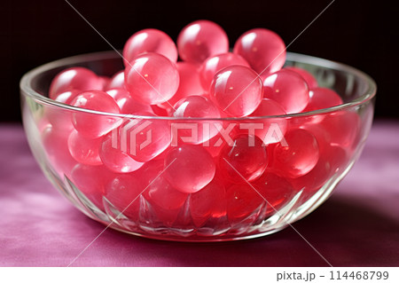 A glass bowl on a table filled with pink chewing jelly candies in sphere round shape closeup shot. Sweet snack dessert 114468799