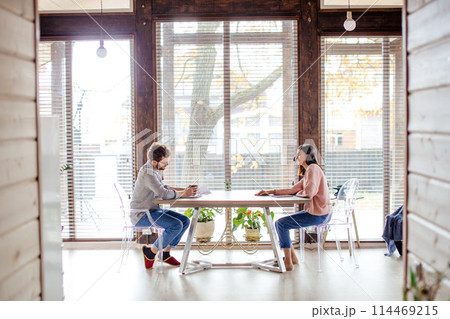 Couple sharing ideas, sitting opposite near big window. 114469215