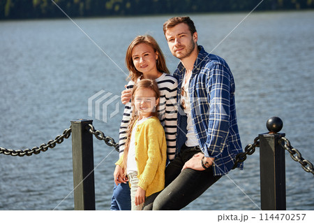 Happy Family looking at camera while posing on pier at quiet lake 114470257