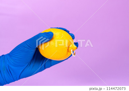 Intimate piercing. Minimal piercing concept. Lemon with piercing on purple background Intimate piercing. Minimal piercing concept. Lemon with piercing on purple background 114472073