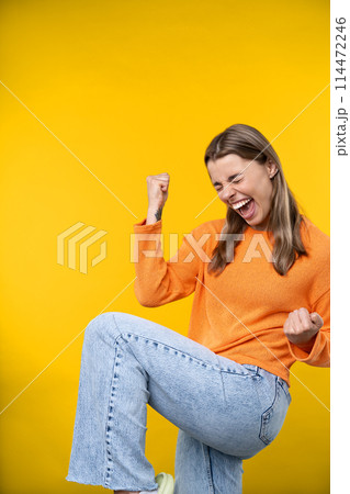 Happy emotions concept. Positive and beautiful young woman laughs poisitively looks aside with carefree face expression wears casual orange sweater isolated over yellow studio background. 114472246