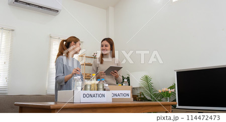 Happy young woman volunteer collecting, sorting food for needy people, team working together on donation project in charitable at home 114472473