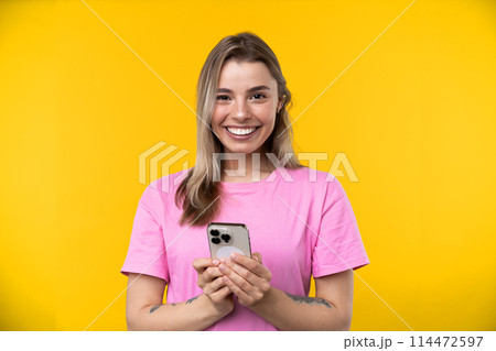 Happy emotions concept. Positive and beautiful young woman laughs poisitively looks aside with carefree face expression wears casual orange sweater isolated over yellow studio background. Happy emotions concept. Positive and beautiful young woman laughs poisitively looks aside with carefree face expression wears casual orange sweater isolated over yellow studio background. 114472597