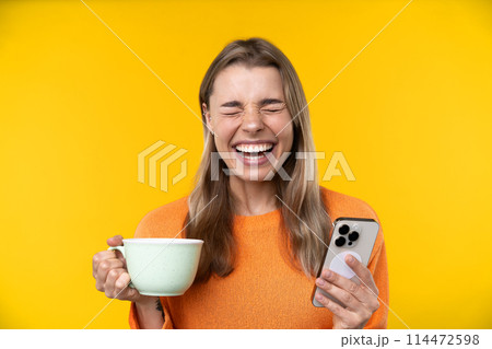 Happy emotions concept. Positive and beautiful young woman laughs poisitively looks aside with carefree face expression wears casual orange sweater isolated over yellow studio background. 114472598