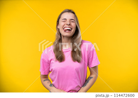 Happy emotions concept. Positive and beautiful young woman laughs poisitively looks aside with carefree face expression wears casual orange sweater isolated over yellow studio background. 114472600