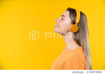 Happy emotions concept. Positive and beautiful young woman laughs poisitively looks aside with carefree face expression wears casual orange sweater isolated over yellow studio background. 114472602