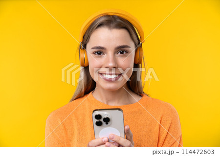Happy emotions concept. Positive and beautiful young woman laughs poisitively looks aside with carefree face expression wears casual orange sweater isolated over yellow studio background. 114472603