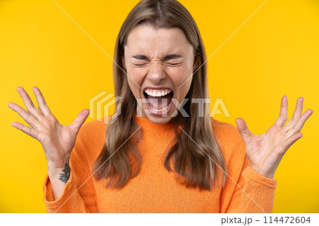 Happy emotions concept. Positive and beautiful young woman laughs poisitively looks aside with carefree face expression wears casual orange sweater isolated over yellow studio background. 114472604