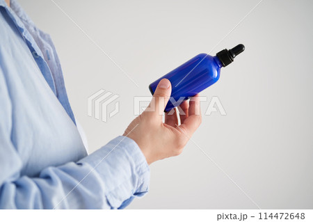 Female hands in a blue shirt hold a blue bottle of serum. 114472648