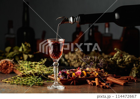 Brown herbal liquor or balm is poured from a vintage bottle into a glass. 114472667